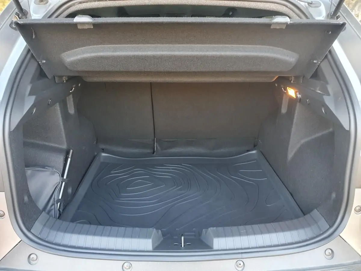 Coffre ouvert vu de l'arrière du Dacia Duster gris schiste, avec tapis de sol noir et éclairage intérieur allumé.