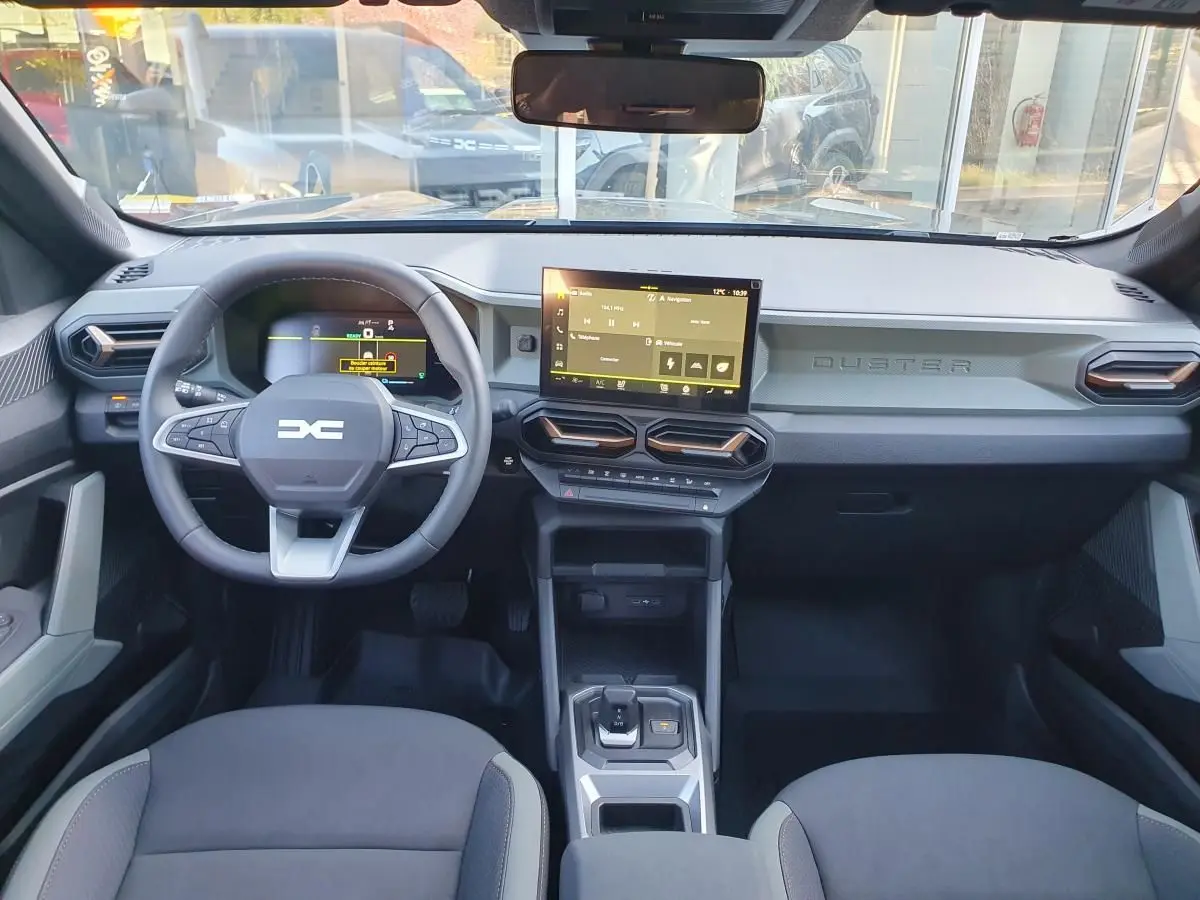 Vue intérieure frontale du tableau de bord du Dacia Duster 2026, avec écran tactile central et volant multifonction.
