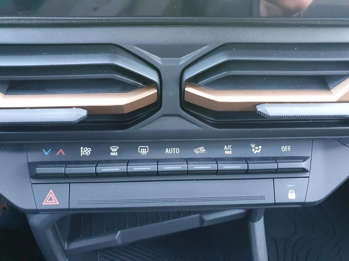 Détail de la console centrale du Dacia Duster 2026 montrant les commandes de climatisation automatique et les aérateurs noirs avec inserts bronze.