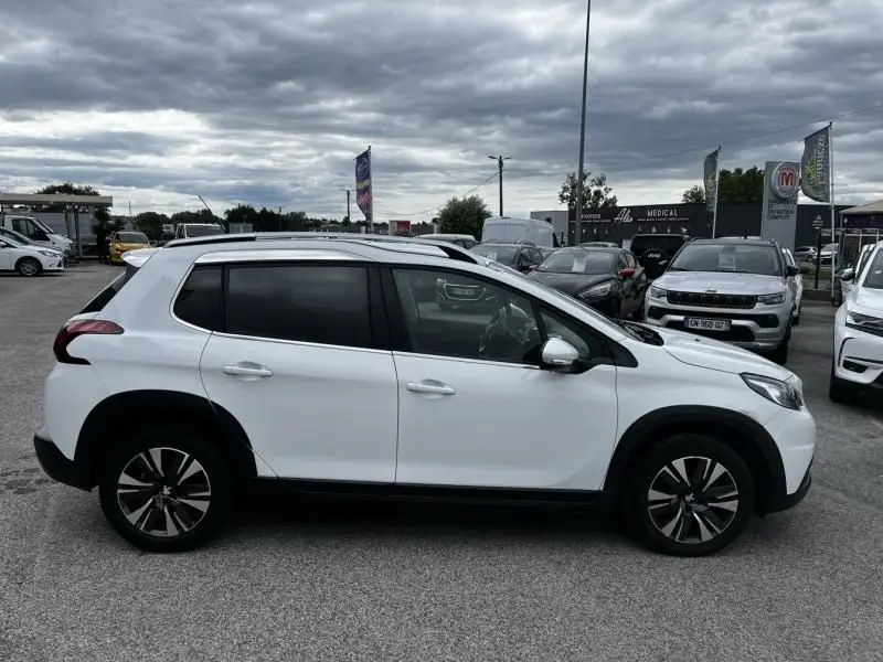 Profil droit d’un Peugeot 2008 blanc de 2019 avec jantes alliage et vitres teintées, stationné en extérieur sous un ciel nuageux.