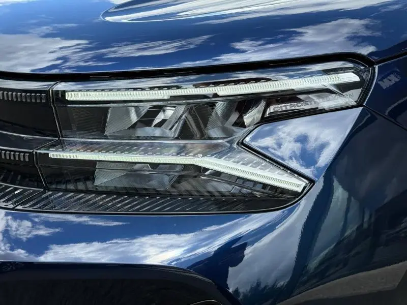 Gros plan sur le phare avant droit bleu métallisé du Citroën C5 Aircross 2025 hybride avec signature lumineuse distinctive.