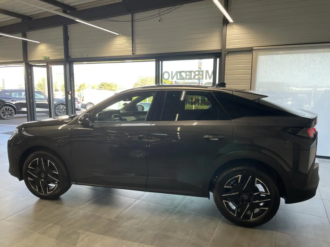 Profil côté gauche du Peugeot 3008 gris foncé hybride 2025 en intérieur, avec jantes alliage 19'' diamantées noires.