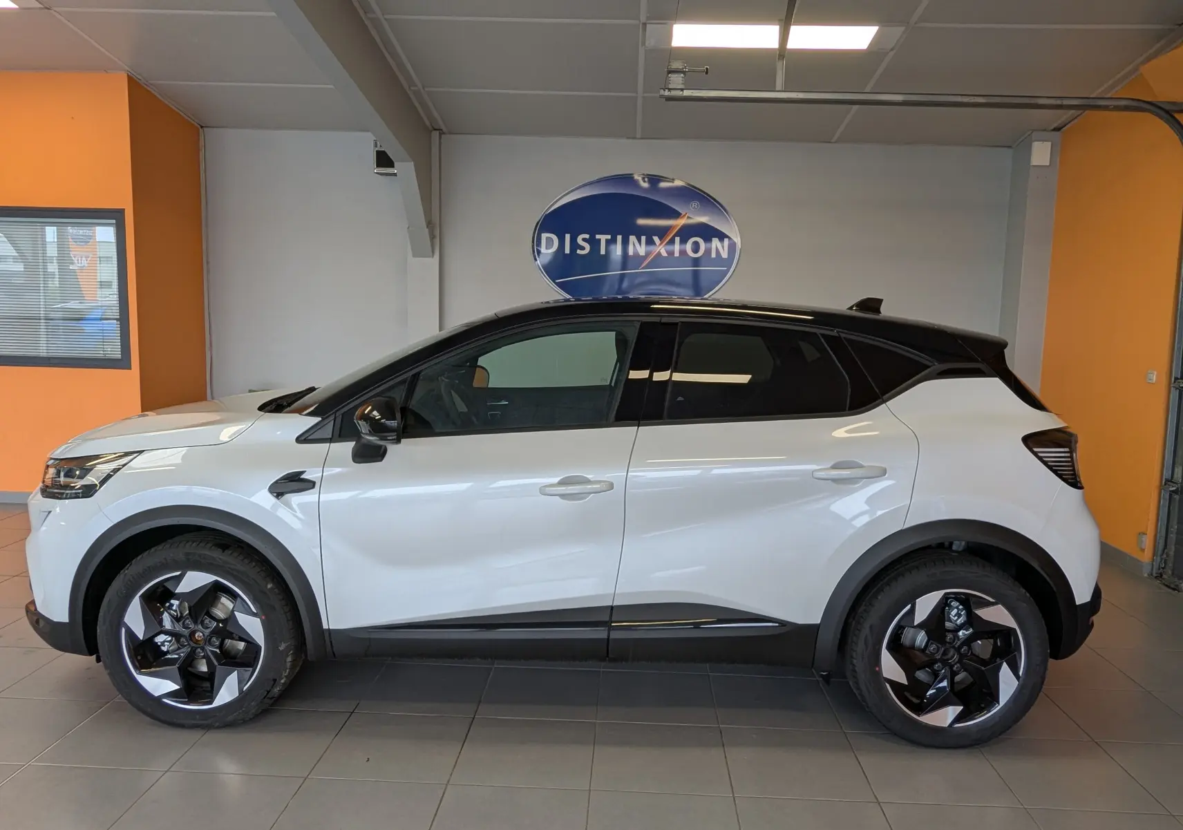 Profil droit du Renault Captur E-Tech Full Hybrid 160ch 2025 blanc nacré avec toit noir et jantes bicolores en showroom.