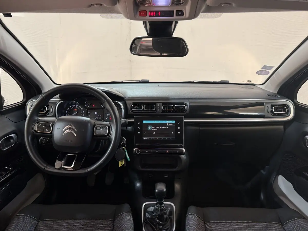 Vue frontale de l'intérieur noir du tableau de bord et volant cuir d'une Citroën C3 Shine Business 2019.