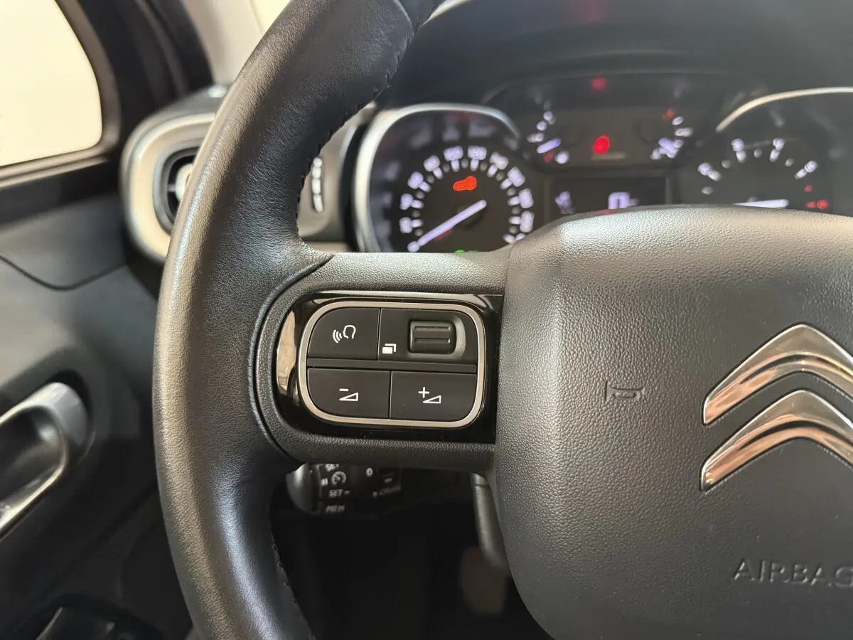 Gros plan sur le volant cuir noir de la Citroën C3 2019 avec commandes audio et tableau de bord en arrière-plan flou.