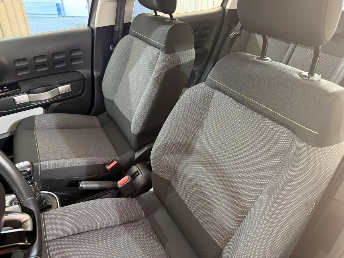 Vue intérieure rapprochée sur les sièges avant gris foncé de la Citroën C3 avec coutures jaunes et poignée de frein à main.