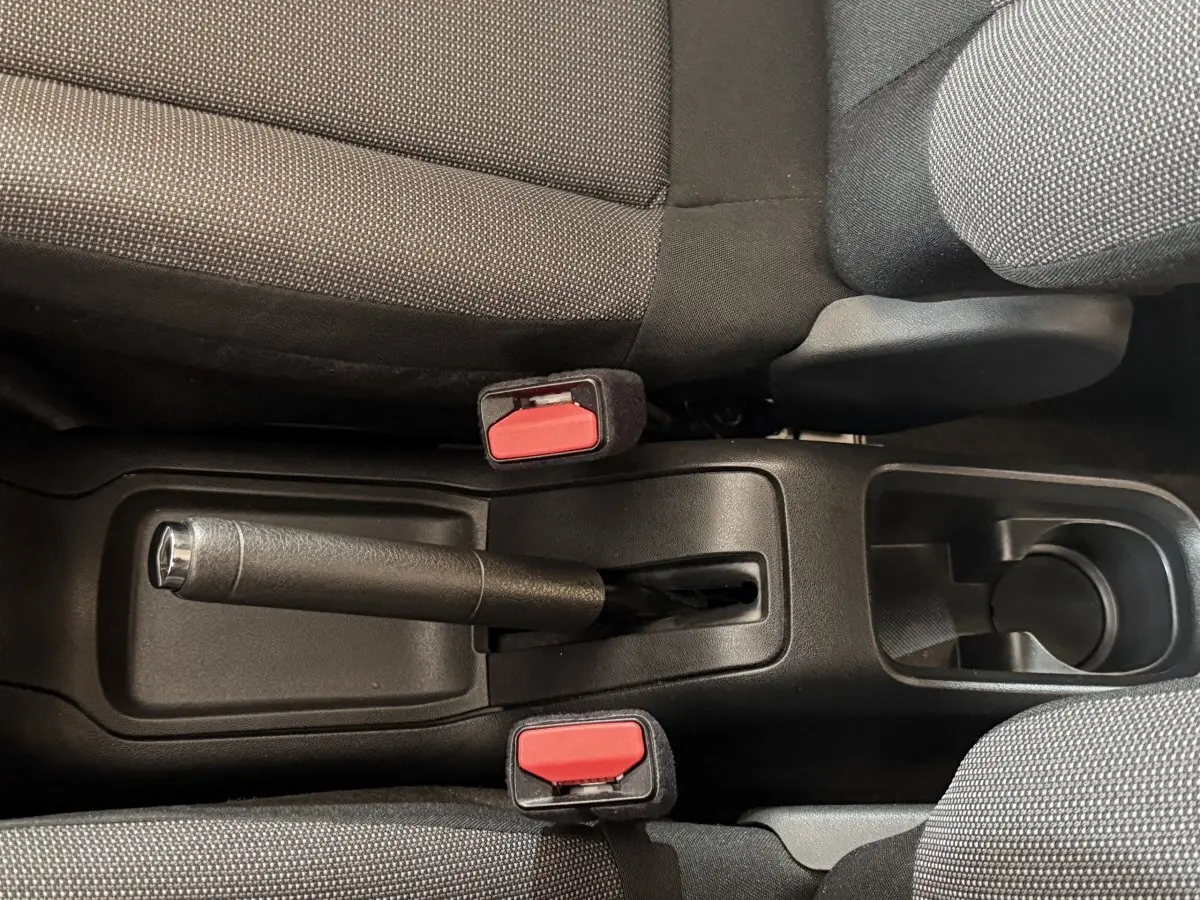 Vue plongeante sur la console centrale noire avec frein à main et ceintures rouges entre sièges gris foncé du Citroën C3.