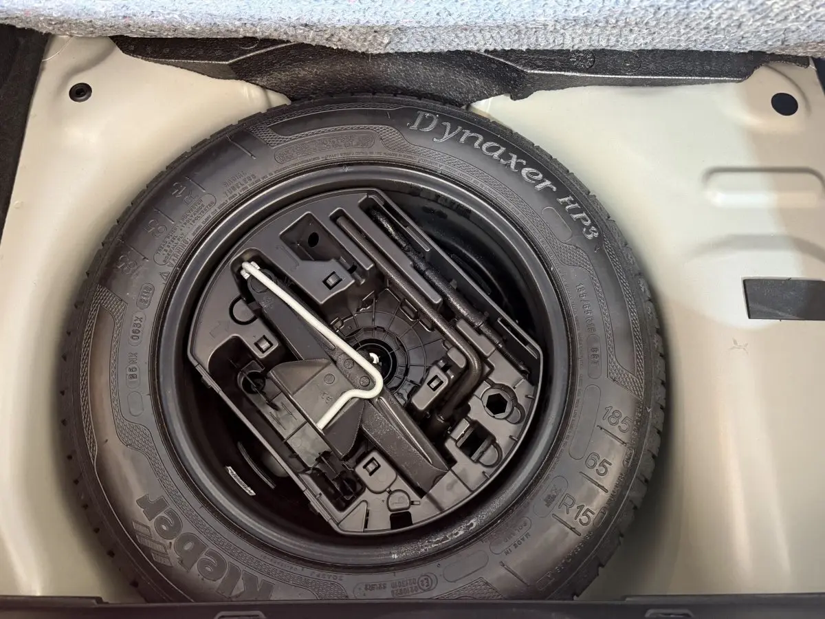 Gros plan sur la roue de secours noire et ses outils dans le coffre gris clair d'une Citroën C3 2019 Shine Business.