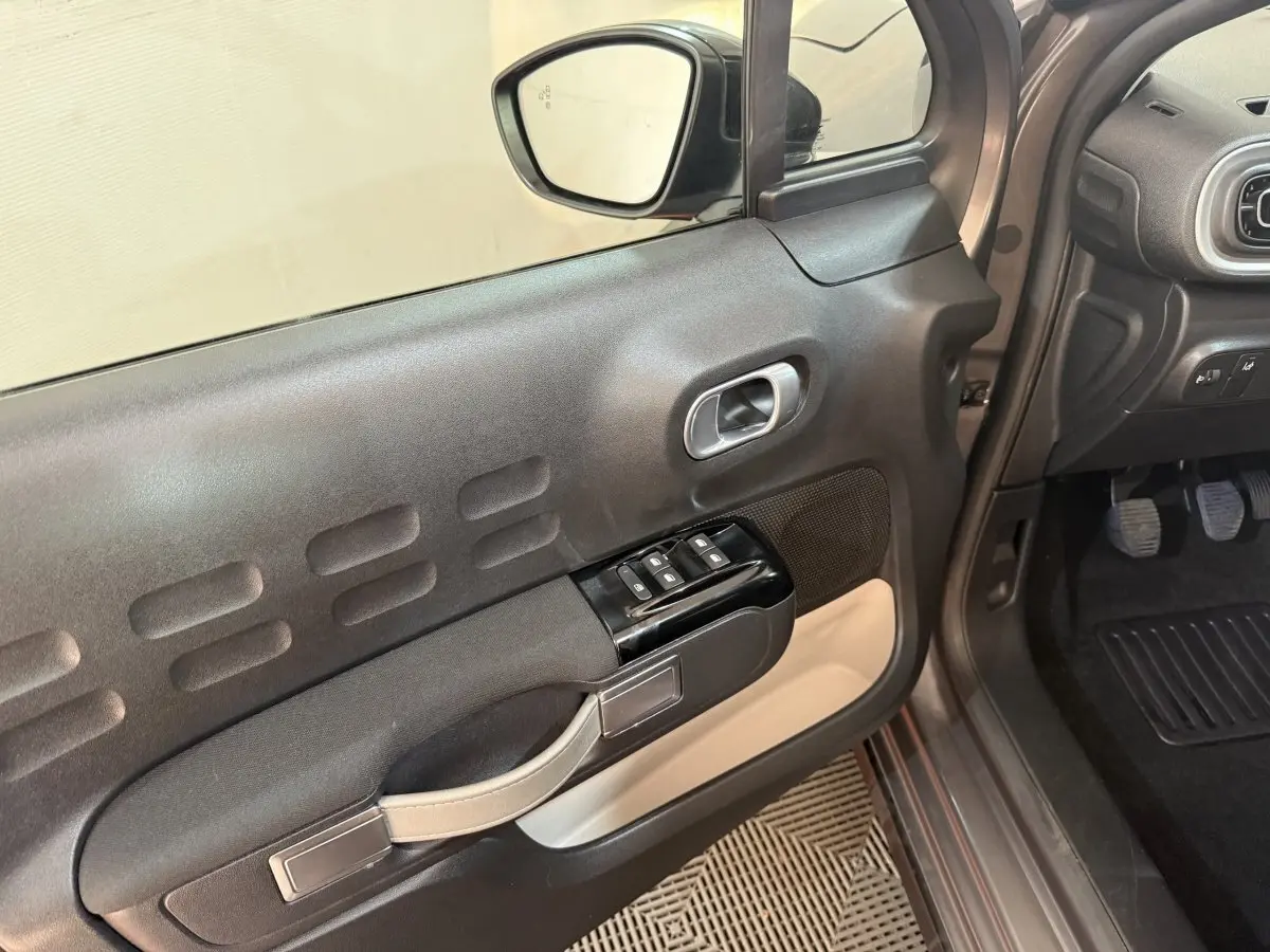 Vue intérieure côté conducteur de la porte noire et beige de la Citroën C3 gris clair avec commandes des vitres et rétroviseur.