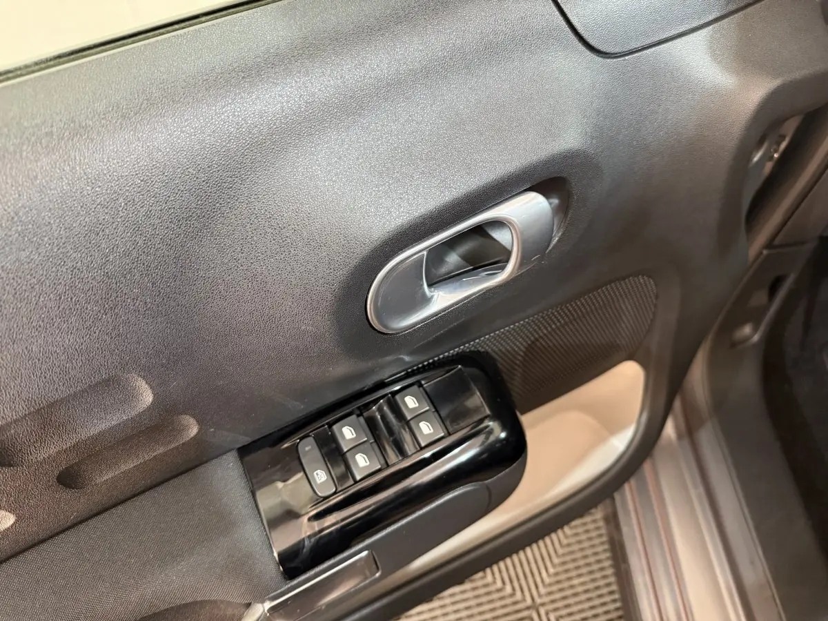 Gros plan sur la commande des vitres et la poignée intérieure côté gauche d'une Citroën C3 gris clair 2019.