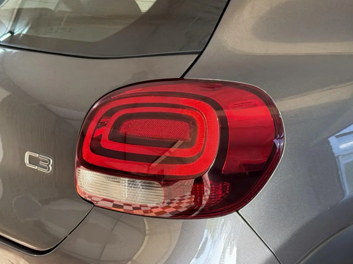 Gros plan sur le feu arrière droit rouge et blanc d'une Citroën C3 gris clair, avec logo C3 visible sur la carrosserie.