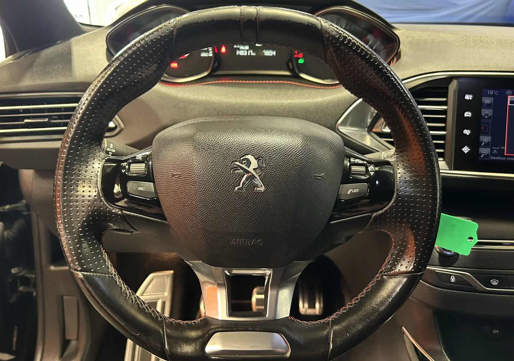 Vue rapprochée du volant en cuir noir perforé de la Peugeot 308 GT Line 2017 avec tableau de bord et écran tactile visibles.