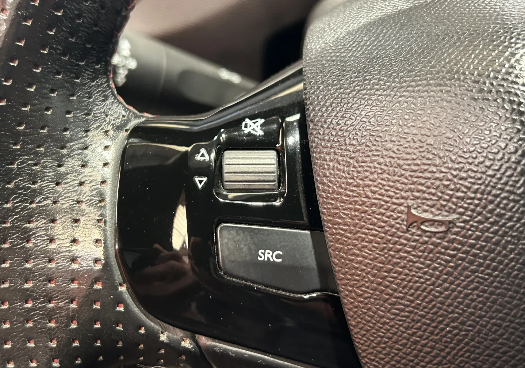 Gros plan sur les commandes noires du volant perforé côté gauche du Peugeot 308 noir, avec bouton SRC et molette sonore.