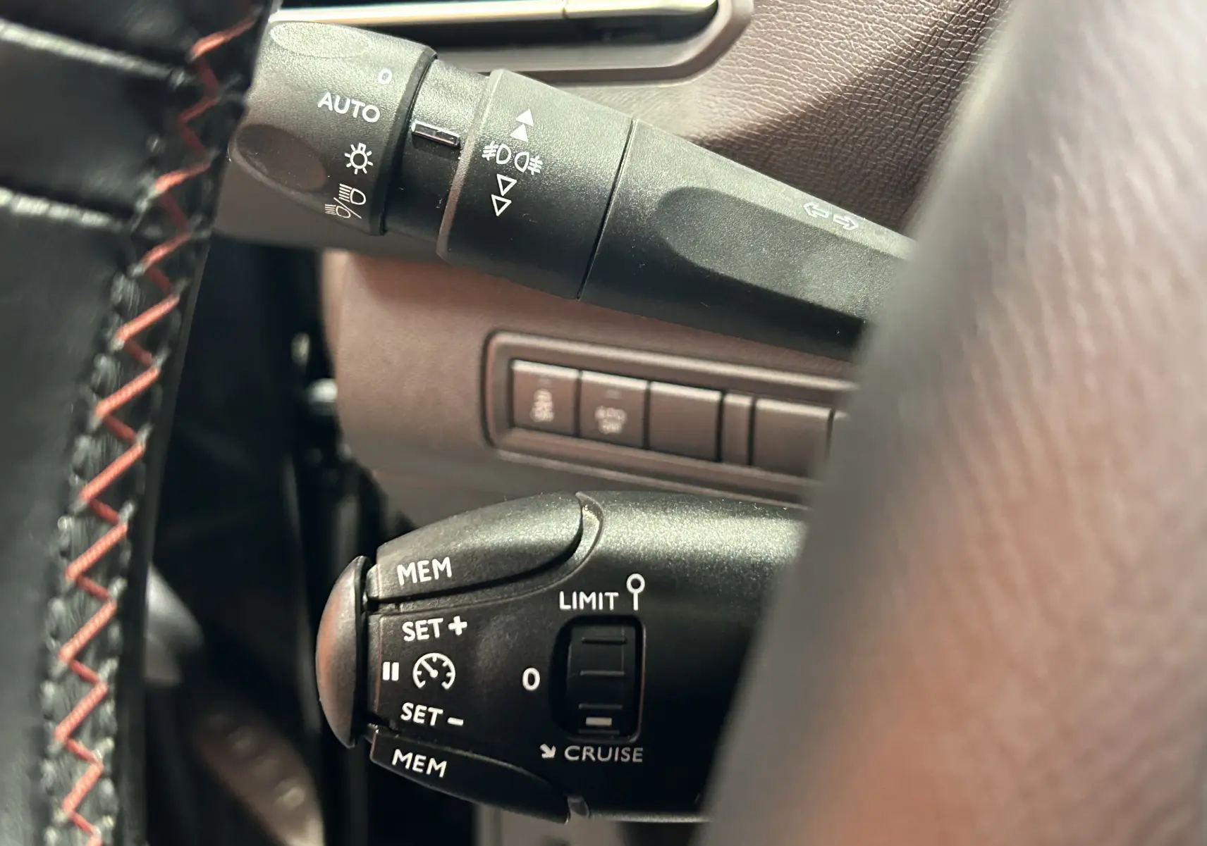 Gros plan sur les commandes de régulateur et feux, volant cuir noir avec surpiqûres rouges, intérieur Peugeot 308 noir.
