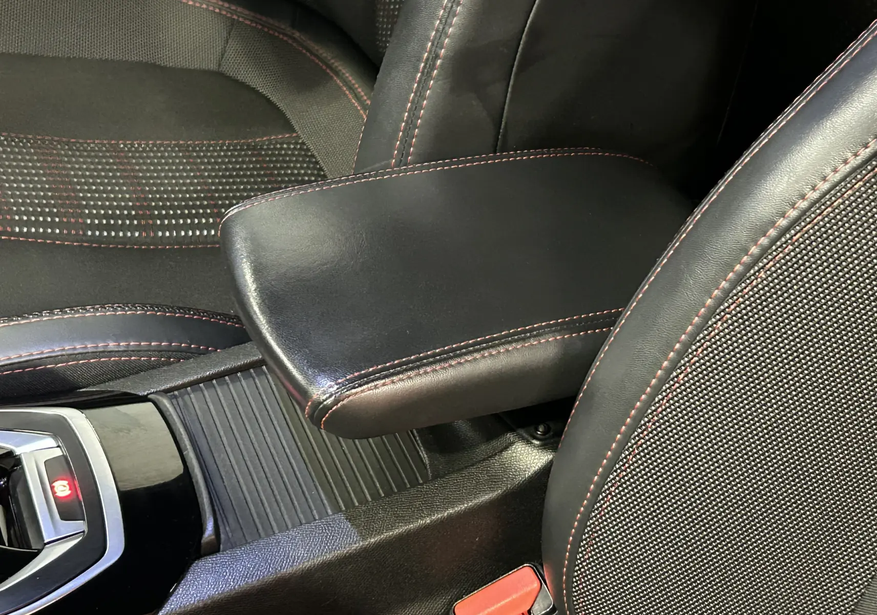 Gros plan intérieur sur l'accoudoir en cuir noir avec surpiqûres rouges entre les sièges avant d'une Peugeot 308 noire.