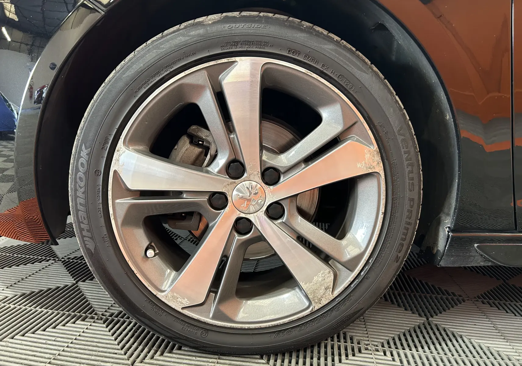 Gros plan sur la roue avant gauche d'une Peugeot 308 noire, jante alliage 5 branches avec traces d'usure visibles.