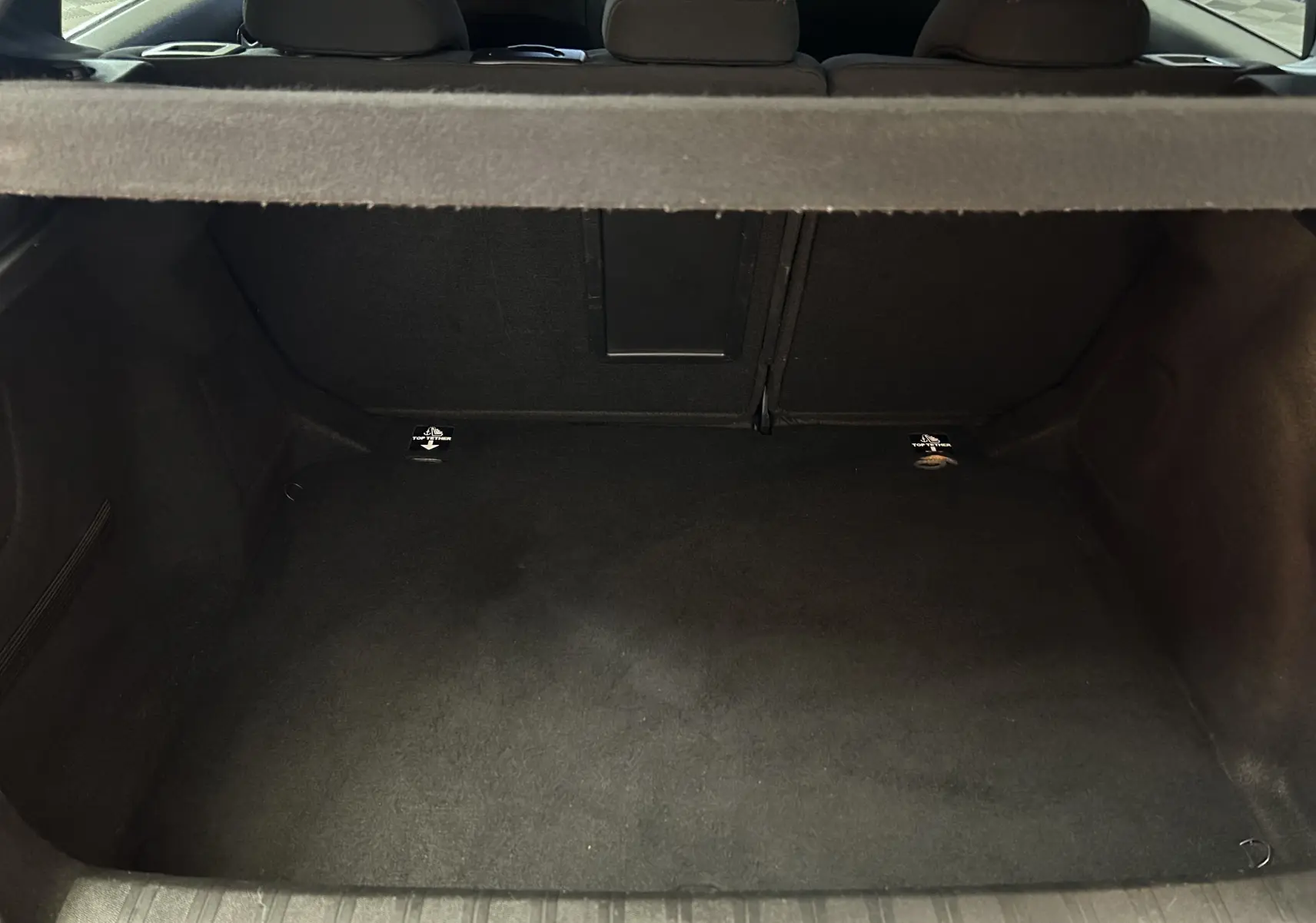 Coffre vide vu de l'arrière d'une Peugeot 308 noire, montrant l'espace de chargement et la banquette arrière.