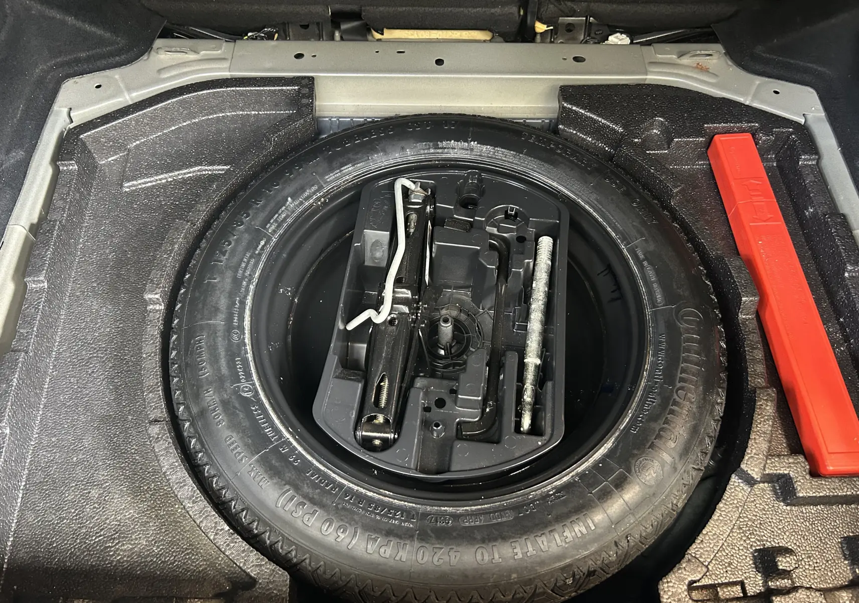 Vue plongeante sur la roue de secours noire et ses outils dans le coffre d'une Peugeot 308 noire de 2017.