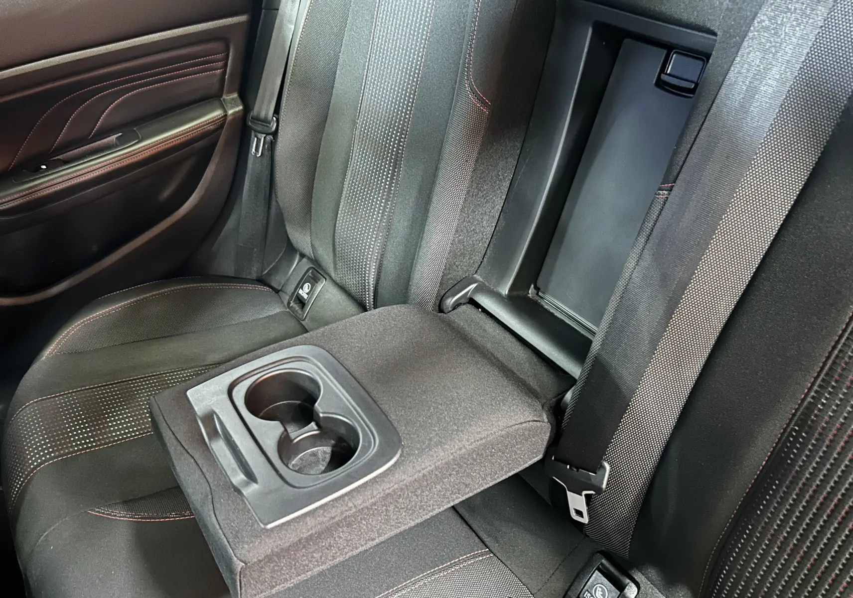 Vue rapprochée de la banquette arrière noire de la Peugeot 308 GT Line avec accoudoir central et porte-gobelets déployés.