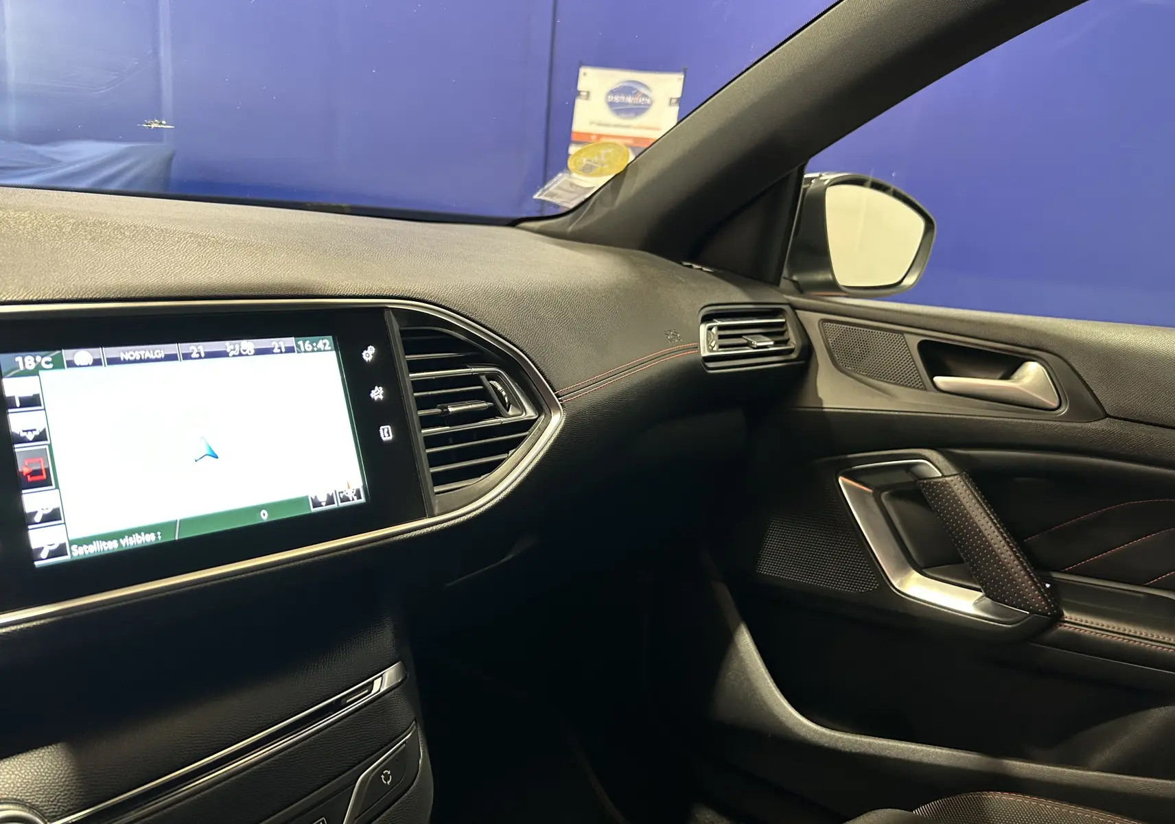 Vue intérieure côté passager de la Peugeot 308 noire, avec écran GPS tactile et finitions en cuir noir et surpiqûres rouges.
