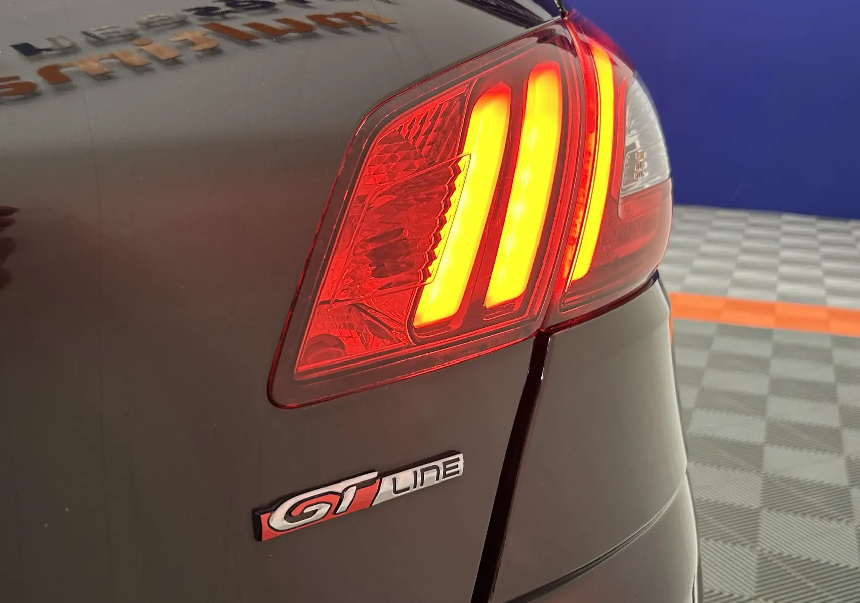 Gros plan sur le feu arrière droit allumé d'une Peugeot 308 GT Line noire, avec logo GT Line visible sur le hayon.