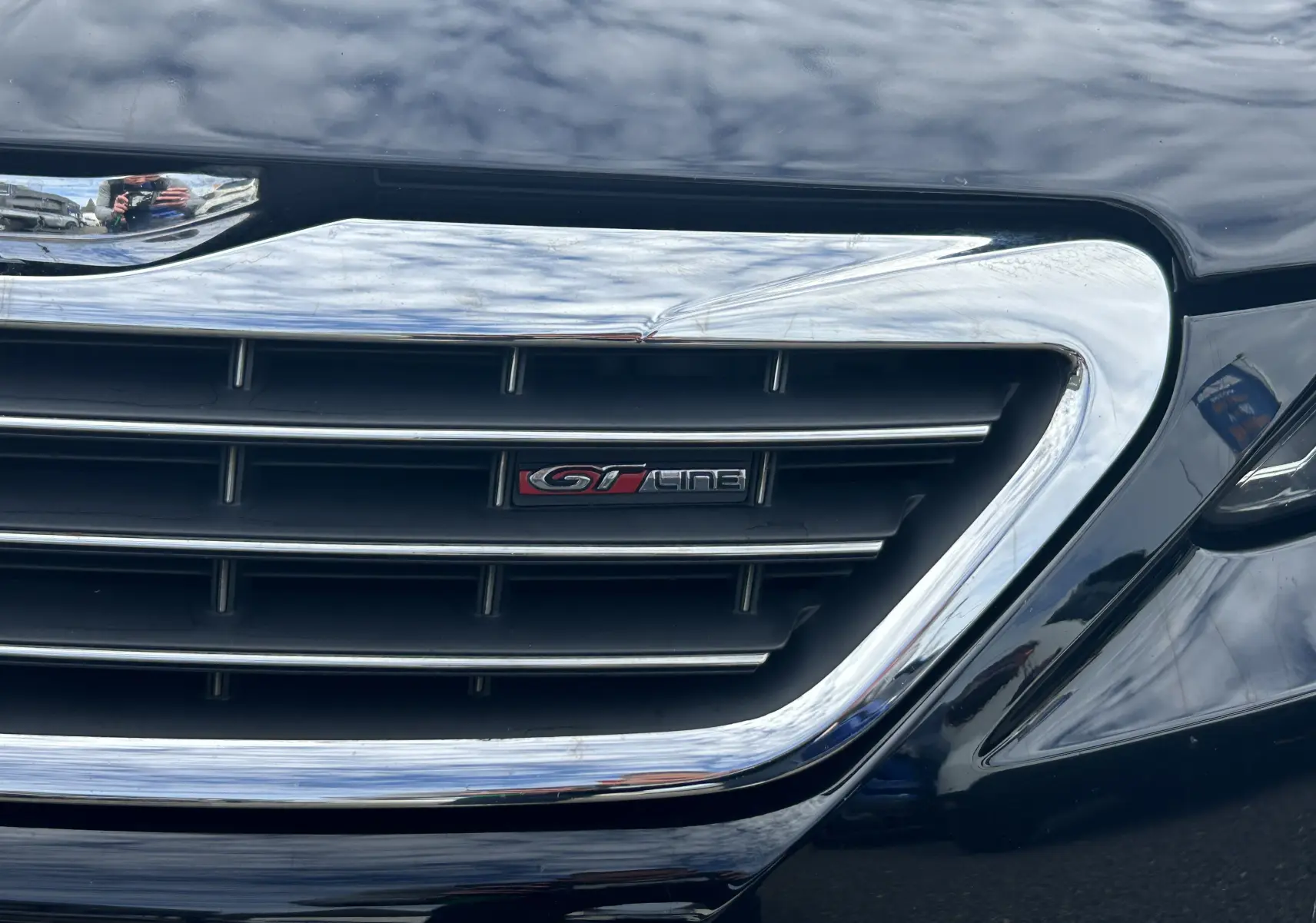 Gros plan sur la calandre chromée noire d'une Peugeot 308 GT Line avec logo distinctif rouge et noir.