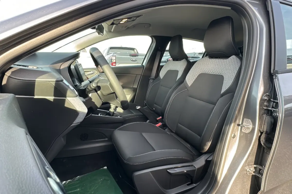 Vue intérieure côté conducteur de la Renault Clio gris schiste 2025, sièges avant bi-matière avec surpiqûres blanches.