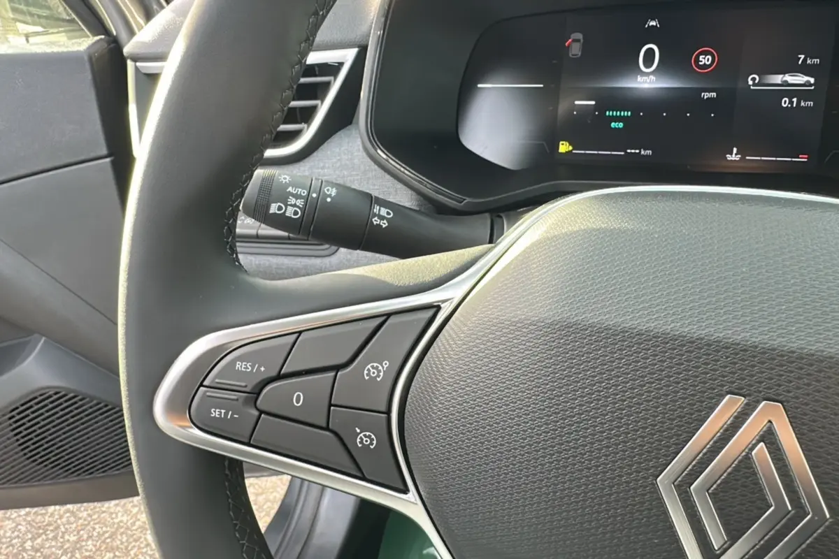 Gros plan sur le volant multifonctions de la Renault Clio gris schiste, avec commandes de régulateur et tableau de bord numérique.