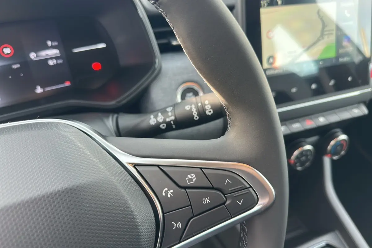 Gros plan sur le volant cuir multifonctions de la Renault Clio gris schiste avec commandes au volant et tableau de bord numérique.