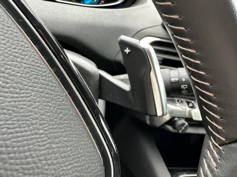 Gros plan sur la palette de changement de vitesse + côté droit du volant cuir noir avec surpiqûres rouges du Peugeot 3008 hybride 2024.