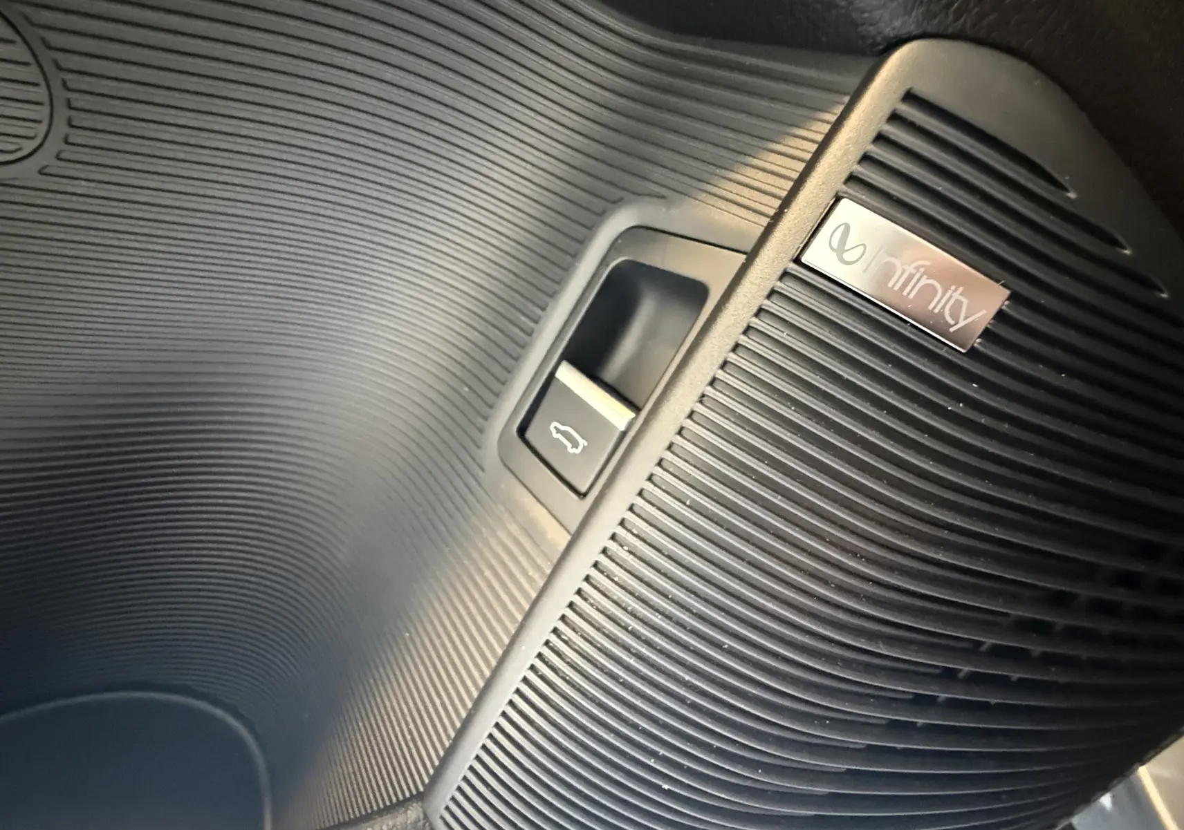 Détail intérieur montrant le bouton d'ouverture du coffre et le haut-parleur Infinity sur la garniture noire.