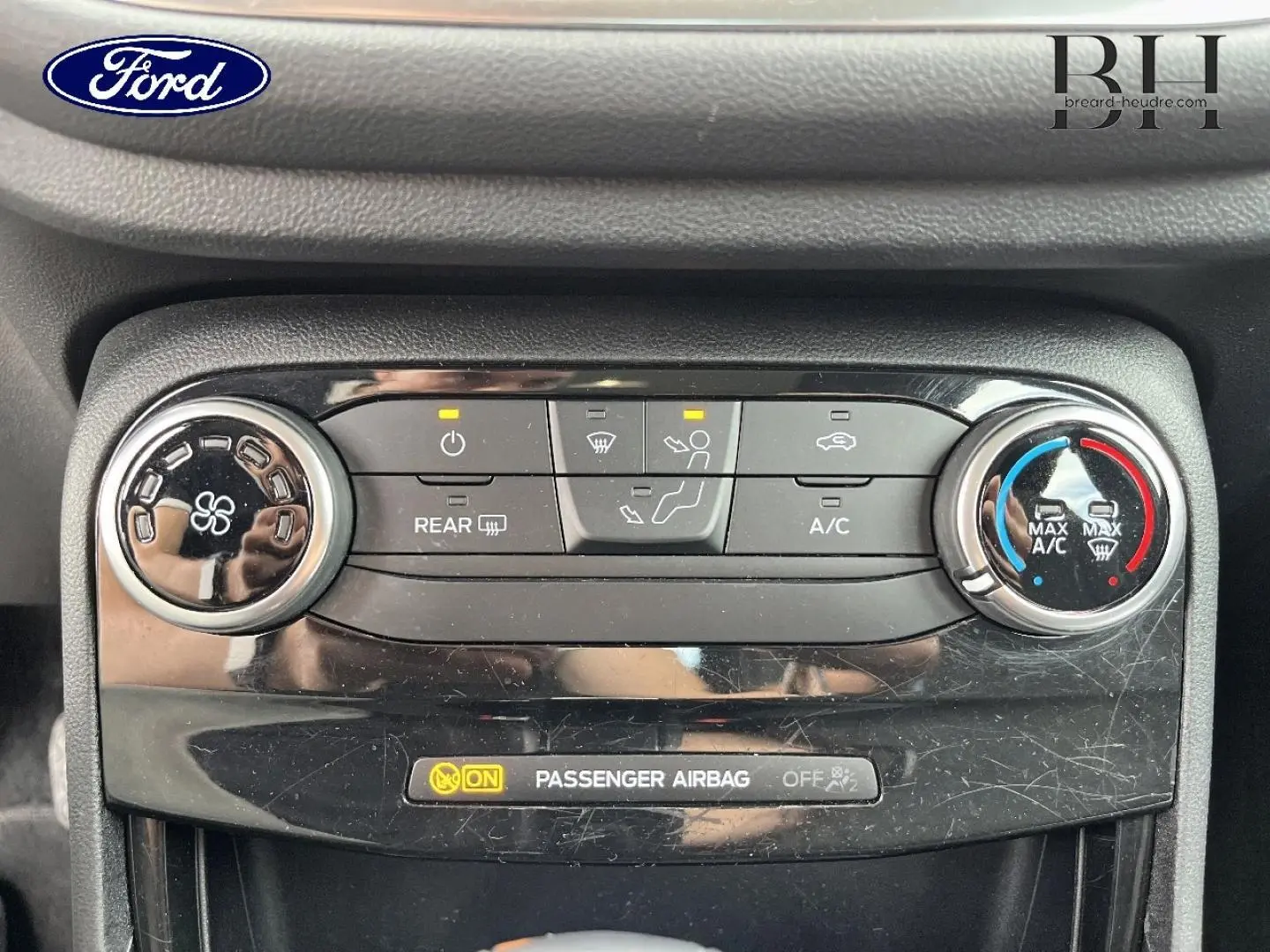 Gros plan sur la console de climatisation d’une Ford Puma bleu, avec commandes circulaires et affichage airbag passager.