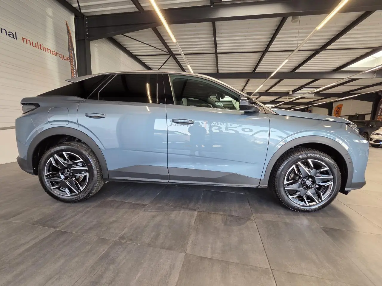 Vue de profil côté gauche du Peugeot 3008 hybride 2025 bleu clair avec jantes alliage 19'' noir brillant en intérieur showroom.