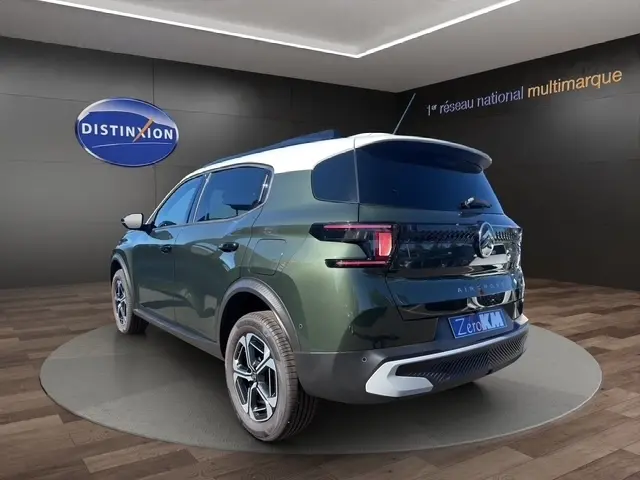 Vue 3/4 arrière droite d'un Citroën C3 Aircross hybride vert avec toit blanc et feux LED, sur podium intérieur showroom.