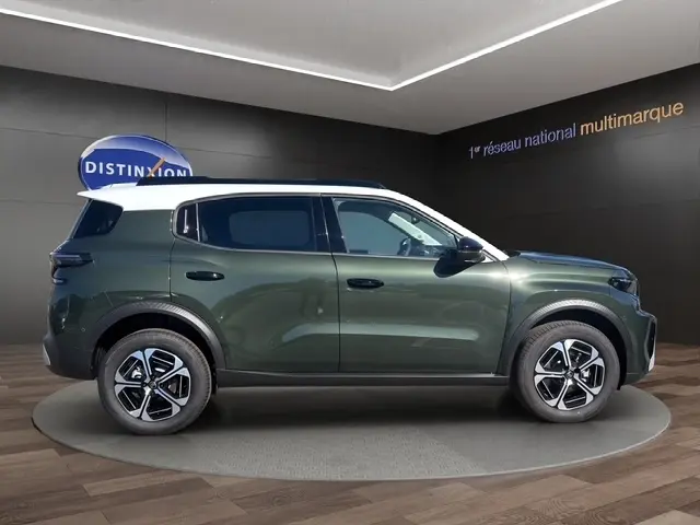 Profil droit d’un Citroën C3 Aircross hybride vert avec toit blanc et jantes modernes, en intérieur showroom.