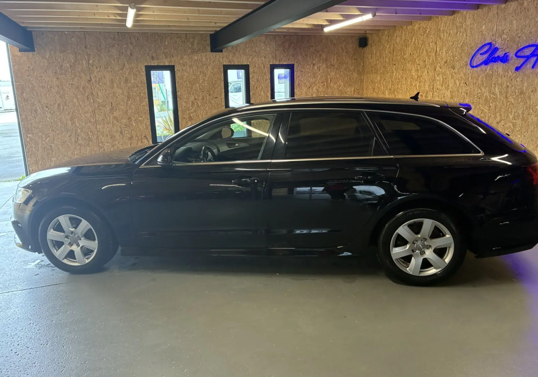 Profil côté gauche d'une Audi A6 Avant noire de 2017, version 2.0 TDI Ambition Luxe, en intérieur sous lumière tamisée.