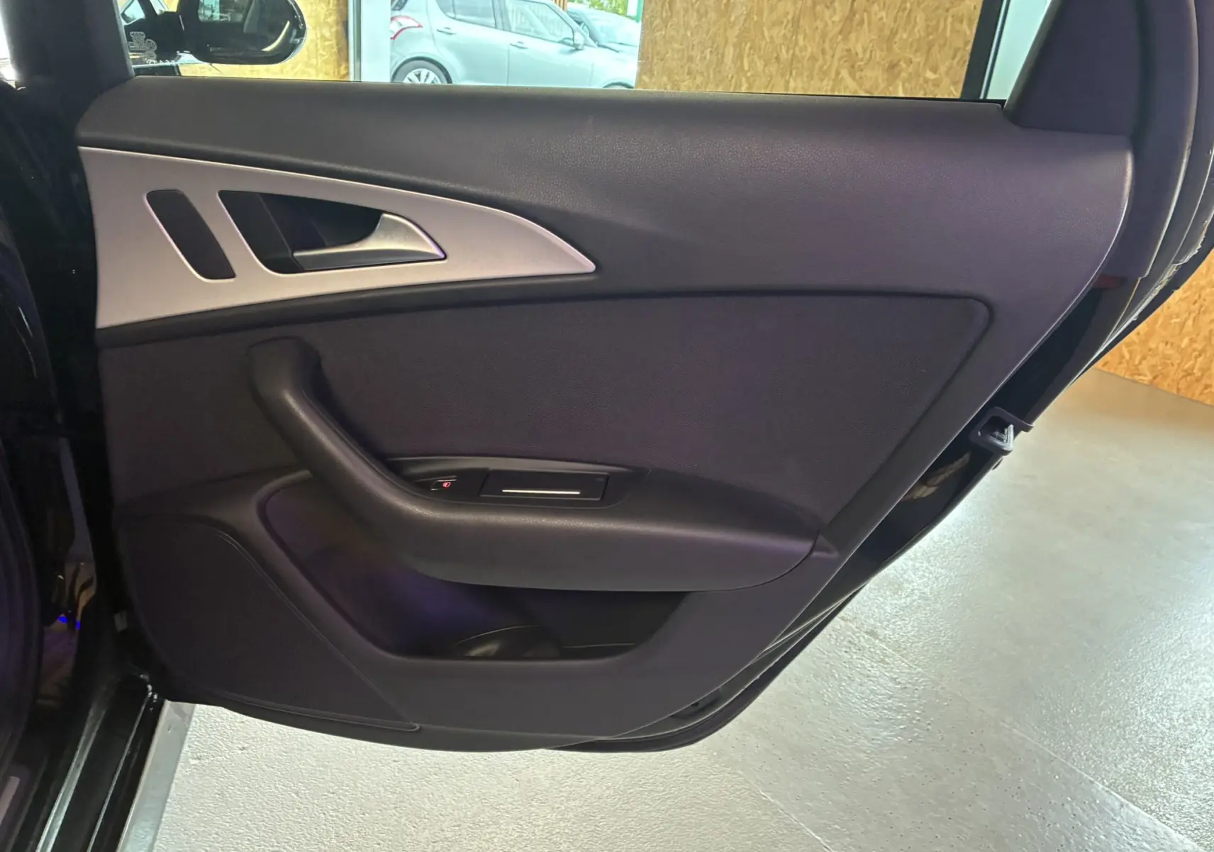 Vue intérieure de la porte arrière gauche noire de l'Audi A6 Avant 2017 avec poignée et commandes de fenêtre intégrées.