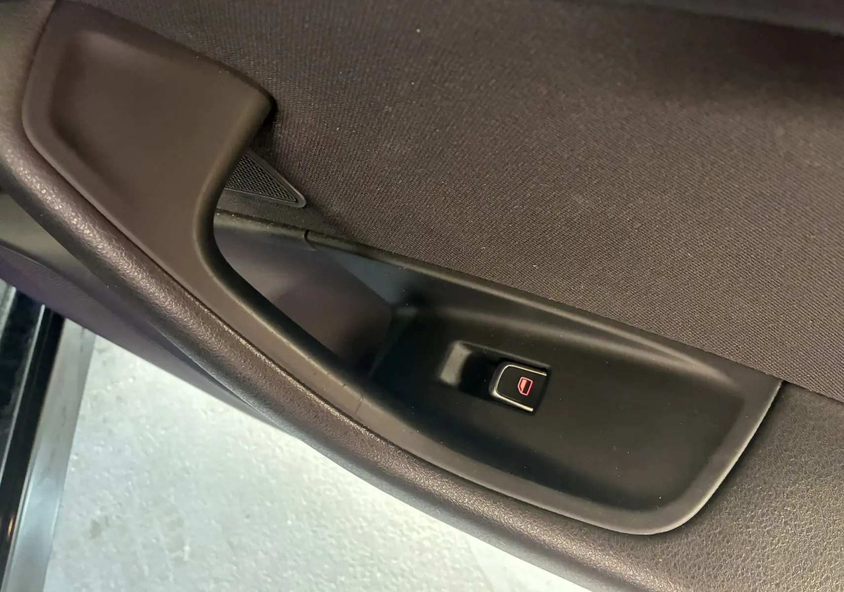 Gros plan sur le bouton de verrouillage électrique des portes côté gauche de l'Audi A6 Avant noire, intérieur tissu noir.