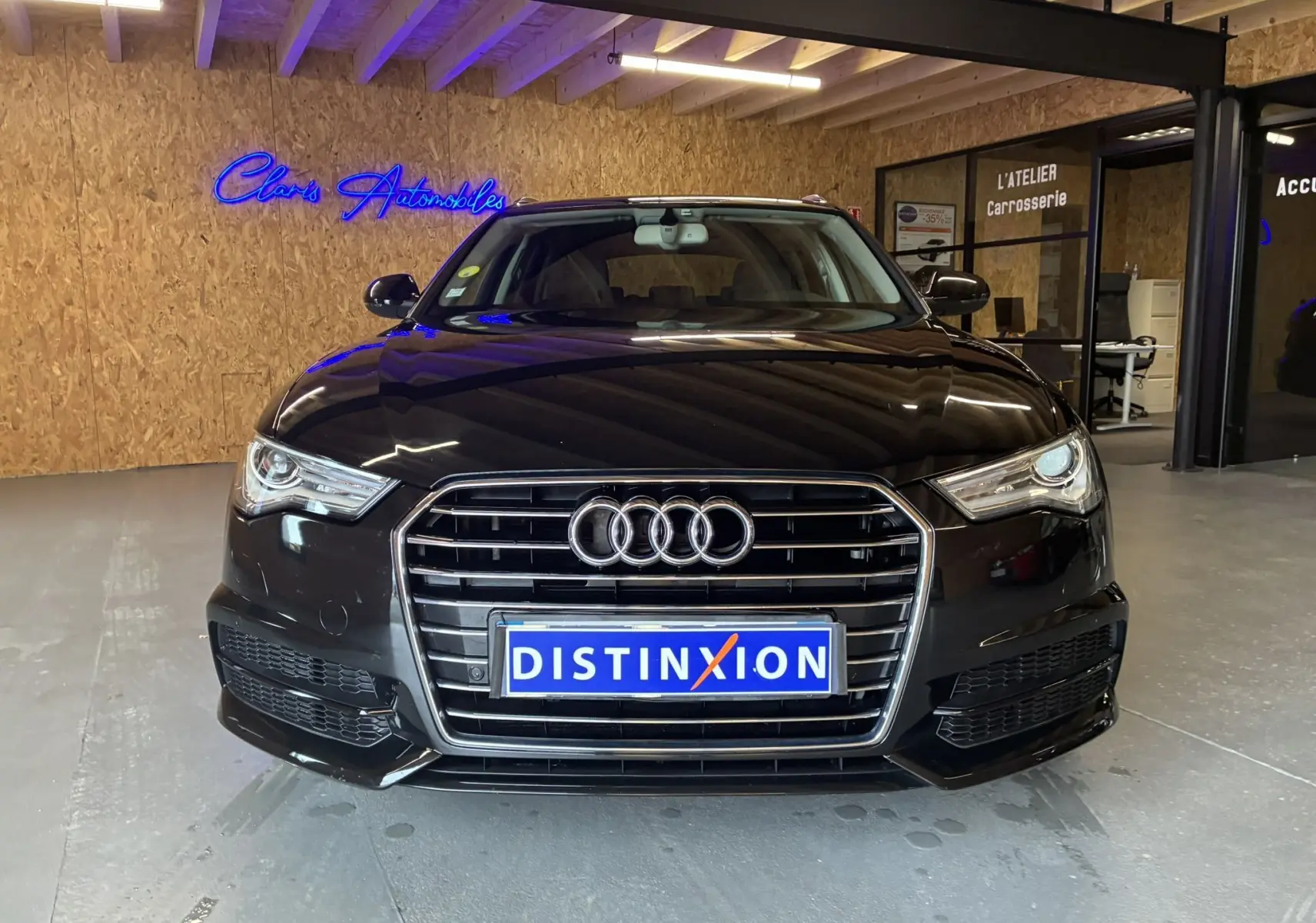 Vue de face d'une Audi A6 Avant noire 2017 avec calandre chromée et logo quatre anneaux, en intérieur showroom.