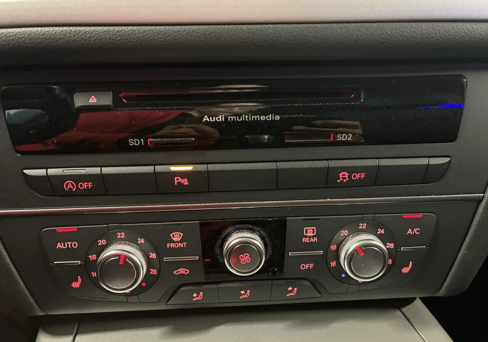 Gros plan sur la console centrale noire de l'Audi A6 Avant 2017, montrant les commandes multimédia et climatisation.