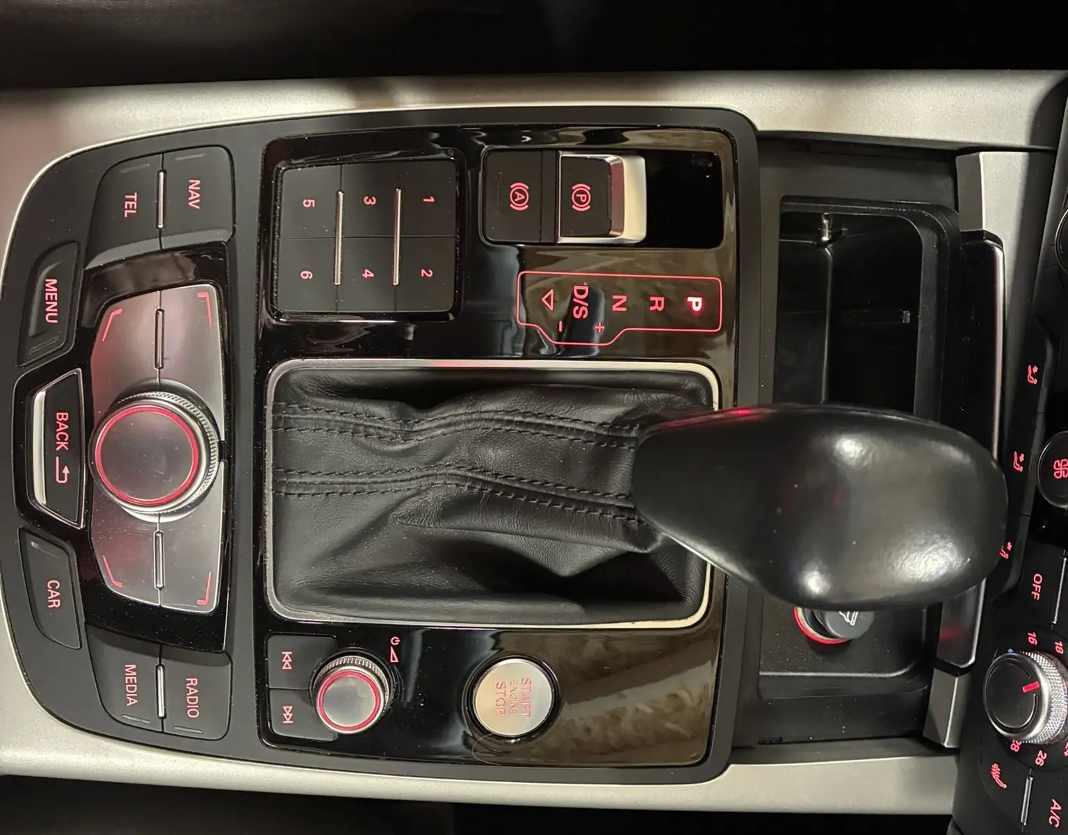 Vue rapprochée de la console centrale noire de l'Audi A6 Avant 2017, avec levier de vitesses automatique et commandes éclairées rouge.