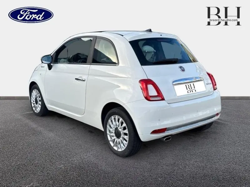 Fiat 500 blanche vue 3/4 arrière droit, avec jantes alu et vitres teintées sur fond neutre.