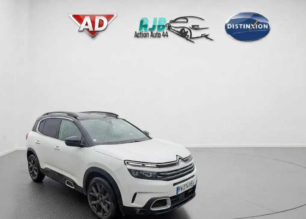 Vue 3/4 avant droite d'un Citroën C5 Aircross blanc nacré avec toit noir et jantes noires en intérieur showroom.