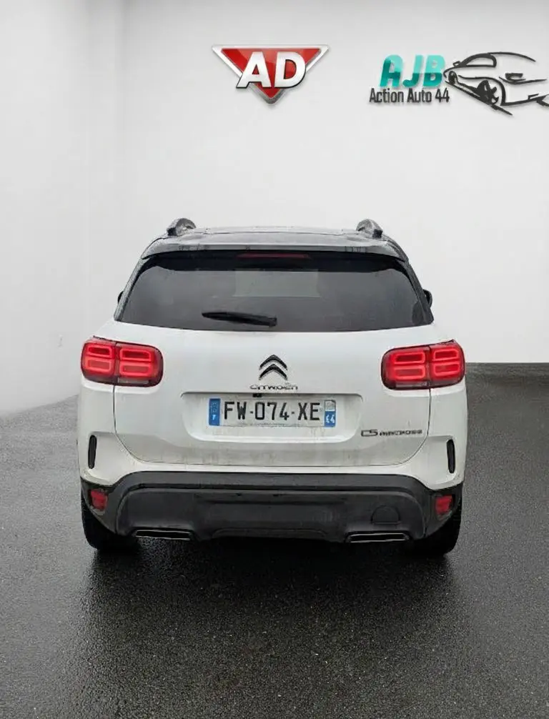 Vue arrière d'un Citroën C5 Aircross blanc nacré avec feux arrière LED allumés dans un showroom.