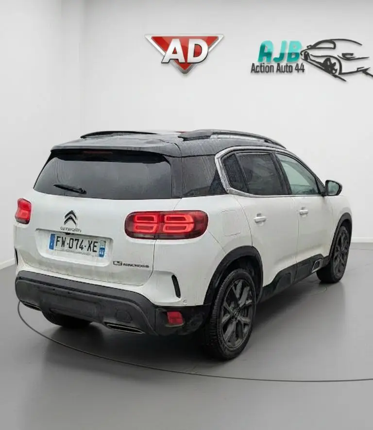Vue 3/4 arrière droite d’un Citroën C5 Aircross blanc nacré avec toit noir et feux arrière LED allumés dans un studio.