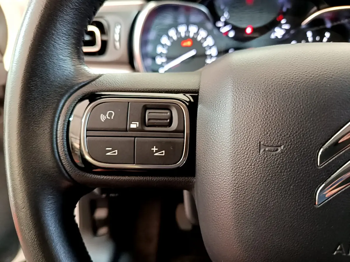 Gros plan sur le volant cuir noir de la Citroën C3 2019 avec commandes audio et tableau de bord lumineux en arrière-plan.