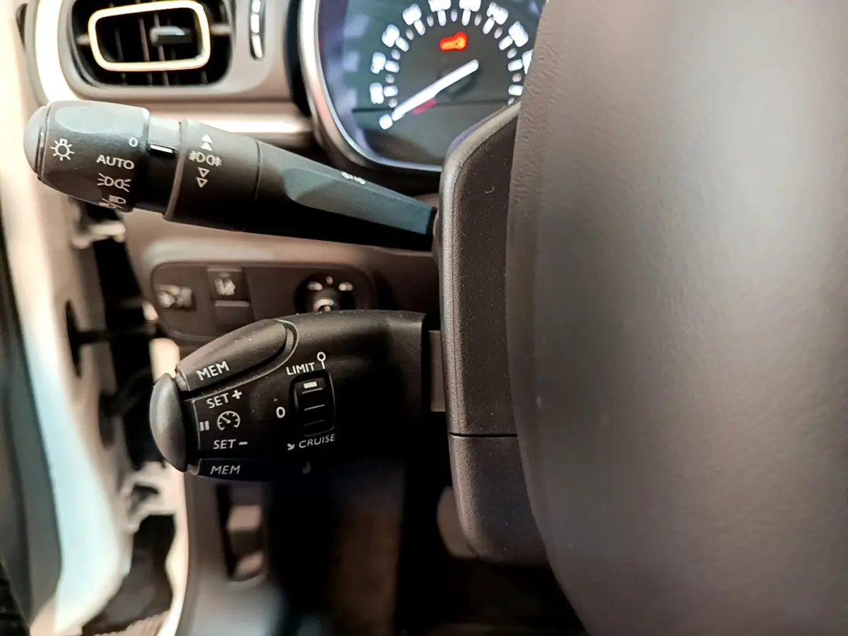 Gros plan sur les commandes de régulateur de vitesse et phares à gauche du volant d'une Citroën C3 blanche de 2019.