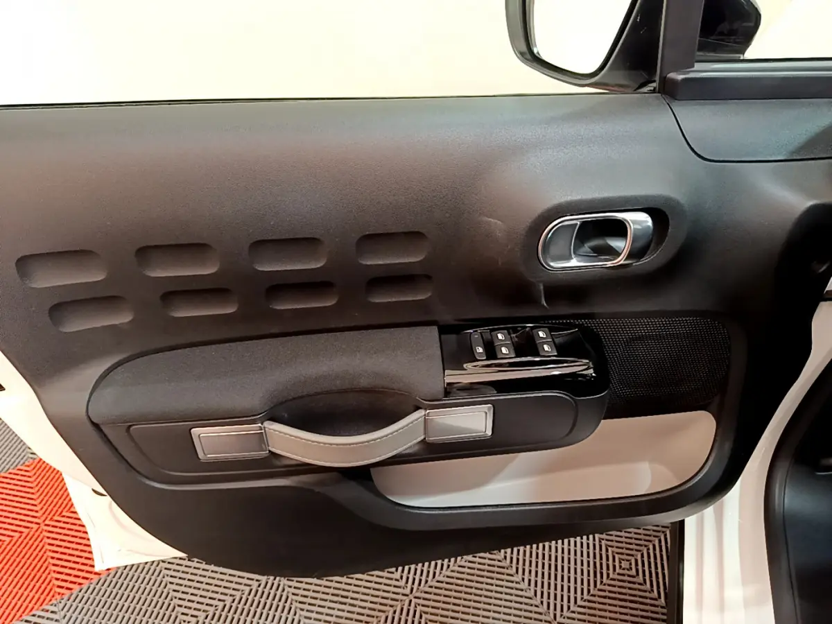 Vue rapprochée de la porte côté gauche d'une Citroën C3 blanche, avec poignée noire et commandes de vitres.