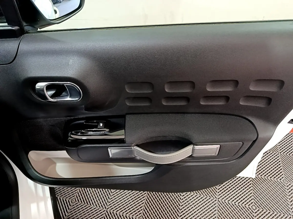 Vue côté gauche de la porte intérieure noire et beige d'une Citroën C3 blanche avec poignée et commandes de vitres.