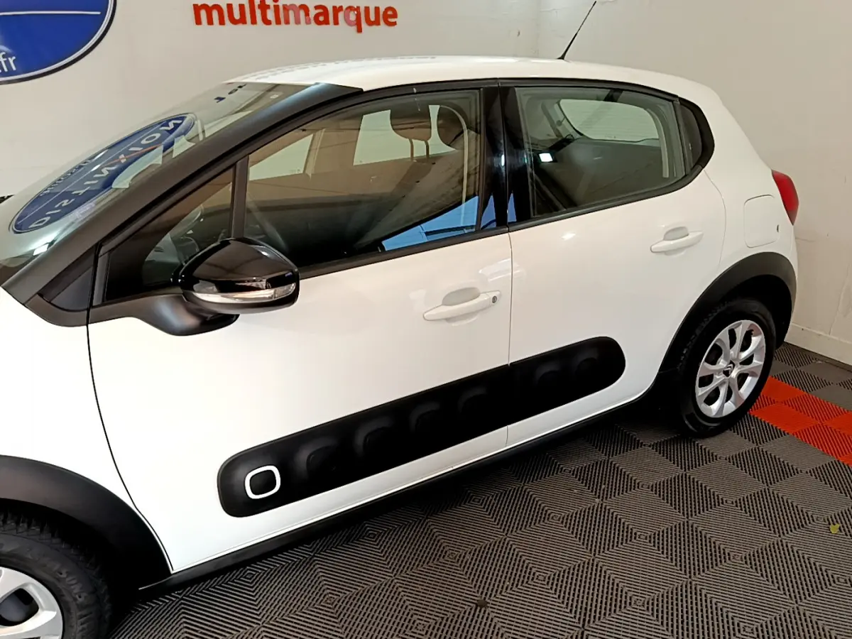 Vue latérale côté gauche d'une Citroën C3 blanche avec protections noires caractéristiques sur les portières.